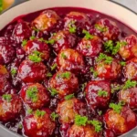Christmas Cranberry Meatballs simmering in a glossy sweet-tart cranberry sauce, garnished with fresh parsley in a festive serving pot.