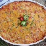 Golden-baked Pimento Cheese Hash Brown Casserole topped with melted cheddar, diced peppers, and sliced jalapeños in a white baking dish.