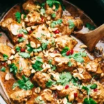 Slow Cooker Peanut Chicken simmering in a creamy peanut sauce topped with cilantro and peanuts