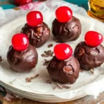 A plate of glossy chocolate-covered Cherry Bourbon Extract Balls topped with bright red cherries and chocolate shavings.