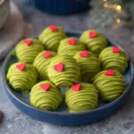 Festive No Bake Grinch Oreo Truffles with green candy coating and red heart sprinkles on a holiday plate.
