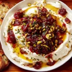 Whipped Feta Dip with Honey Pistachios and Cranberries served in a white bowl, topped with honey drizzle, chopped pistachios, and cranberries, surrounded by toasted bread slices