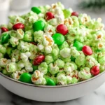 Grinch Popcorn Mix piled high in a white bowl with green candy-coated popcorn and red and green M&Ms, a fun and festive Christmas snack.