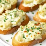 Artichoke Bruschetta with creamy melted cheese and parsley on toasted baguette slices, broiled until golden and bubbly.