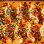 Viral Baked Dumplings from TikTok in a baking dish, baked in creamy coconut curry sauce with chili crisp, sesame seeds, cilantro, and green onions.