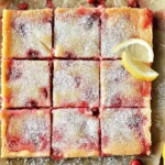 Cranberry Lemon Bars cut into squares, topped with powdered sugar, with fresh cranberries and lemon slices on parchment paper