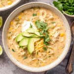 Slow Cooker Creamy Green Chile Chicken Enchilada Soup served with avocado, shredded cheese, cilantro, and lime wedges on the side.