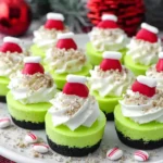 Grinch Mini Cheesecakes topped with whipped cream, crushed cookies, and festive red Santa hat candies on a holiday dessert plate.