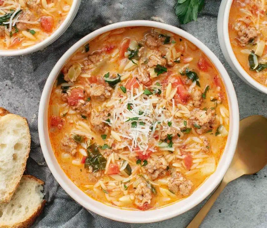 Italian Sausage Orzo Soup served in a white bowl with creamy tomato broth, tender orzo pasta, sausage, spinach, and grated Parmesan