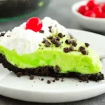 Slice of No Bake Grinch Pie with whipped cream, chocolate chips, and a cherry on an Oreo crust