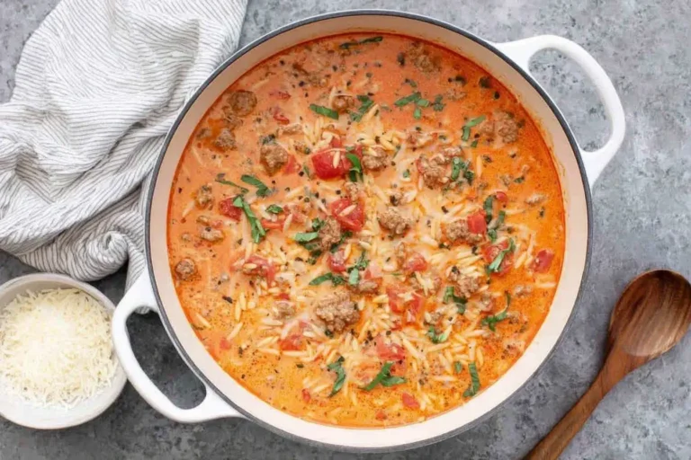 Italian Sausage Orzo Soup simmering in a white Dutch oven with creamy broth, tender orzo, sausage crumbles, tomatoes, and fresh herbs