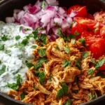 Slow Cooker Chicken Shawarma bowl with shredded spiced chicken, creamy yogurt sauce, fresh tomatoes, red onion, and herbs