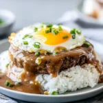 Hawaiian Loco Moco with white rice, juicy beef patty, rich brown gravy, and a sunny-side egg topped with sliced green onions.