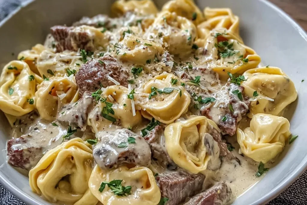 Philly Cheesesteak Tortellini Pasta with steak bites, cheese tortellini, and creamy provolone sauce, topped with fresh herbs in a shallow bowl.