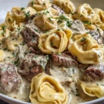 Philly Cheesesteak Tortellini Pasta in a creamy provolone sauce with tender steak bites and herb garnish in a white bowl.