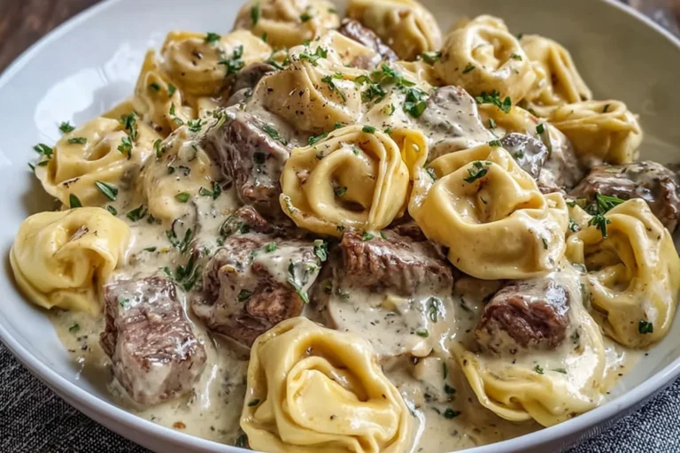 Philly Cheesesteak Tortellini Pasta in a creamy provolone sauce with tender steak bites and herb garnish in a white bowl.