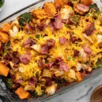 Buffalo Chicken Sweet Potato Casserole in a glass baking dish with roasted sweet potatoes, chicken, broccoli, melted cheddar, bacon, and green onions.