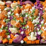 Sheet Pan Buffalo Chicken and Sweet Potato Bowls on a baking sheet with roasted chicken, sweet potatoes, cauliflower, red onion, purple cabbage, feta, and green onions.