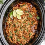Slow cooker filled with shredded Crockpot Cilantro Lime Chicken, topped with fresh cilantro and lime wedges in a rich, saucy tomato base.