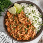 Bowl of Crockpot Cilantro Lime Chicken with shredded saucy chicken, fluffy cilantro rice, and fresh lime wedges.