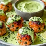 Baked Salmon Meatballs topped with creamy avocado sauce on a plate, garnished with herbs and served with a lime wedge.