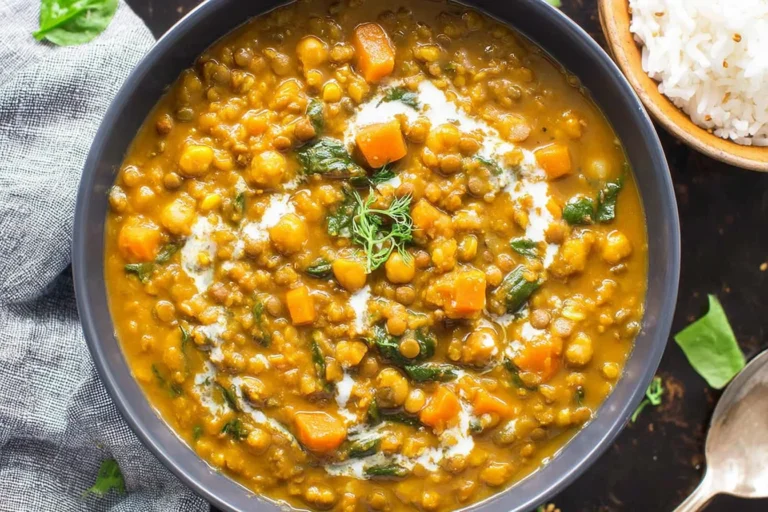 Pumpkin Curry with veggies, lentils, and chickpeas in a bowl, finished with a creamy coconut milk swirl and fresh herbs.