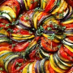 Homemade Classic French Ratatouille in a white baking dish with spiral layers of zucchini, eggplant, tomatoes, and yellow squash in rich tomato sauce.