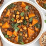 Vegan Moroccan Stew in a white bowl with chickpeas, lentils, sweet potatoes, spinach, and cilantro, served with flatbread on the side.