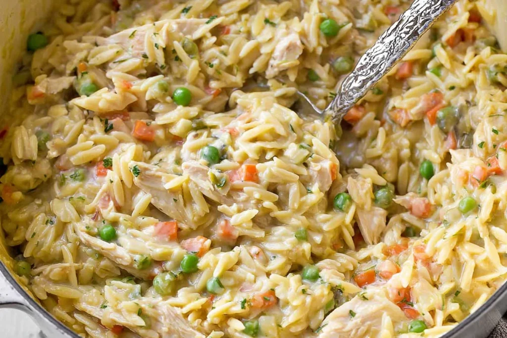 Close-up of Chicken Pot Pie Orzo Recipe—creamy orzo with shredded chicken, peas, carrots, and herbs in a skillet.
