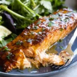 Air Fryer Honey Mustard Salmon fillet glazed and flaky on a plate with lemon wedge, fresh greens, and herbs.
