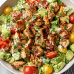 Avocado Chicken Salad in a white bowl with seared chicken bites, creamy avocado chunks, red and yellow cherry tomatoes, fresh cilantro, and a zesty lime dressing.