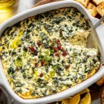Spinach and Pepperoncini Baked Feta Dip in a white baking dish, golden and bubbly with crackers on the side.