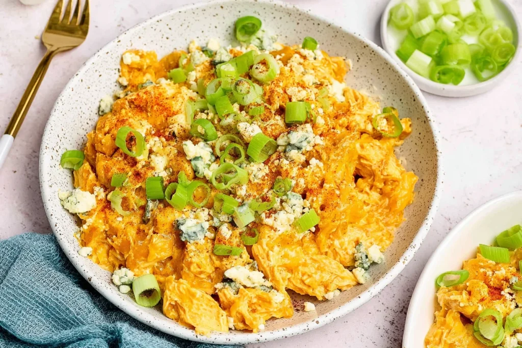 Buffalo Chicken Casserole served in a bowl, creamy and spicy, topped with crumbled blue cheese, sliced green onions, and a sprinkle of seasoning.