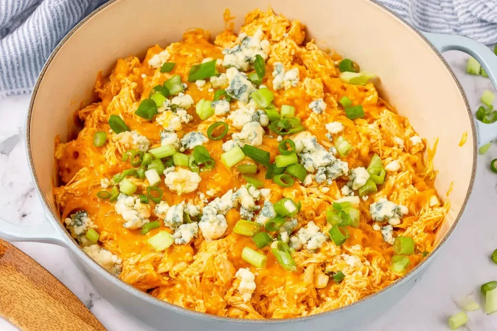 Buffalo Chicken Casserole in a white skillet, creamy and cheesy with blue cheese crumbles and green onions on top.