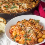 Chicken Parmesan Gnocchi in a skillet with crispy Parmesan breadcrumb topping, marinara sauce, mozzarella, and fresh basil, served with crusty bread.