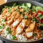 Chicken Crispy Rice Salad with Creamy Peanut Dressing in a bowl with crispy rice, sliced chicken, cucumbers, tomatoes, herbs, and peanut drizzle.
