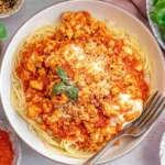 Ground Chicken Parmesan over spaghetti topped with marinara, melted mozzarella, parmesan, and fresh basil in a white bowl.