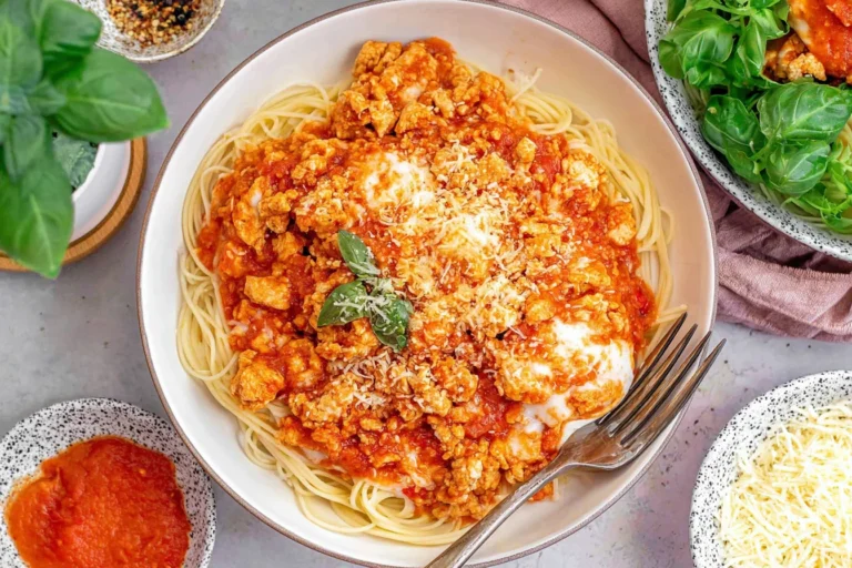 Ground Chicken Parmesan over spaghetti topped with marinara, melted mozzarella, parmesan, and fresh basil in a white bowl.