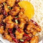 Hot Orange Chicken Panda Express copycat—crispy fried chicken bites coated in sticky spicy orange sauce with dried red chilies, sesame seeds, and rice.