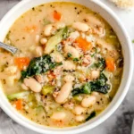 Top-down bowl of Italian White Bean Soup with cannellini beans, sausage, carrots, celery, and spinach, finished with cracked pepper.
