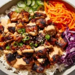 Korean BBQ Chicken Bowls with charred gochujang chicken over white rice, topped with cucumbers, shredded carrots, purple cabbage, sesame seeds, and green onions.