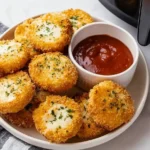 Air Fried Babybel Cheese bites with crispy panko coating, garnished with parsley and served with marinara dip on a plate.