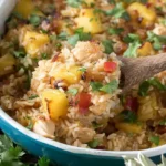 Spoonful of Aloha Pineapple Chicken Rice Casserole with tender chicken, caramelized pineapple, fluffy rice, and fresh cilantro in a baking dish.