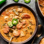 Creamy Cajun White Chicken Chili in a bowl with shrimp, andouille sausage, diced peppers, and fresh jalapeño slices on top.