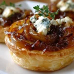Caramelized Onion and Goat Cheese Tarts close-up on a white plate, featuring flaky puff pastry, glossy caramelized onions, goat cheese crumbles, and thyme.