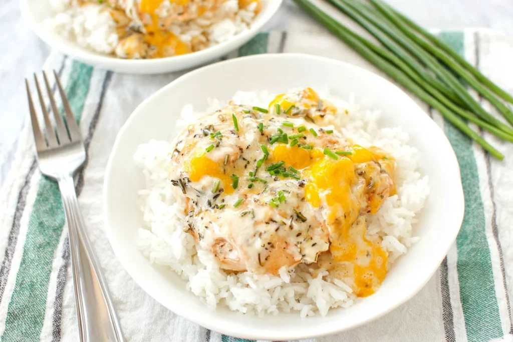 Chicken Olivia served over fluffy white rice with creamy melted cheddar sauce and fresh chives in a white bowl.