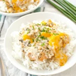 Chicken Olivia served over fluffy white rice with creamy melted cheddar sauce and fresh chives in a white bowl.