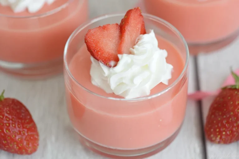 Strawberry Greek Yogurt Jello in a glass topped with whipped cream and fresh strawberry slices on a light wooden table.
