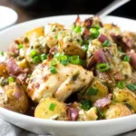 German Fried Potatoes with Chicken in a white bowl—crispy red potatoes, tender chicken, turkey bacon, and green onions in a tangy skillet sauce.