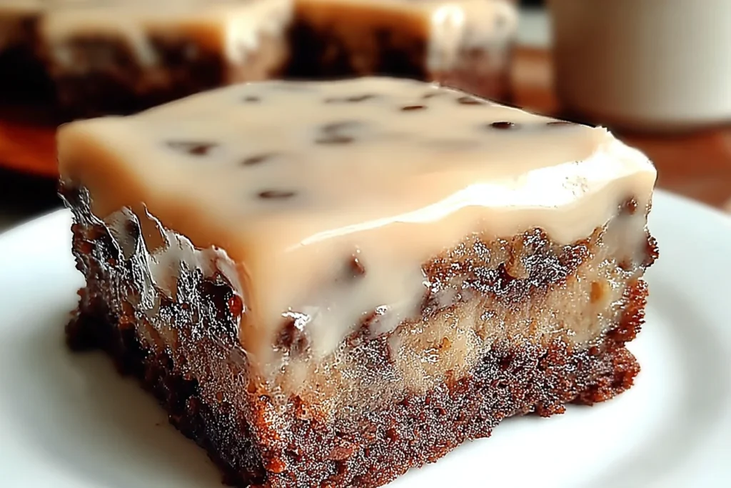 Banana Bread Brownies topped with creamy glaze and chocolate chips on a white plate, showing a fudgy banana-chocolate swirl.